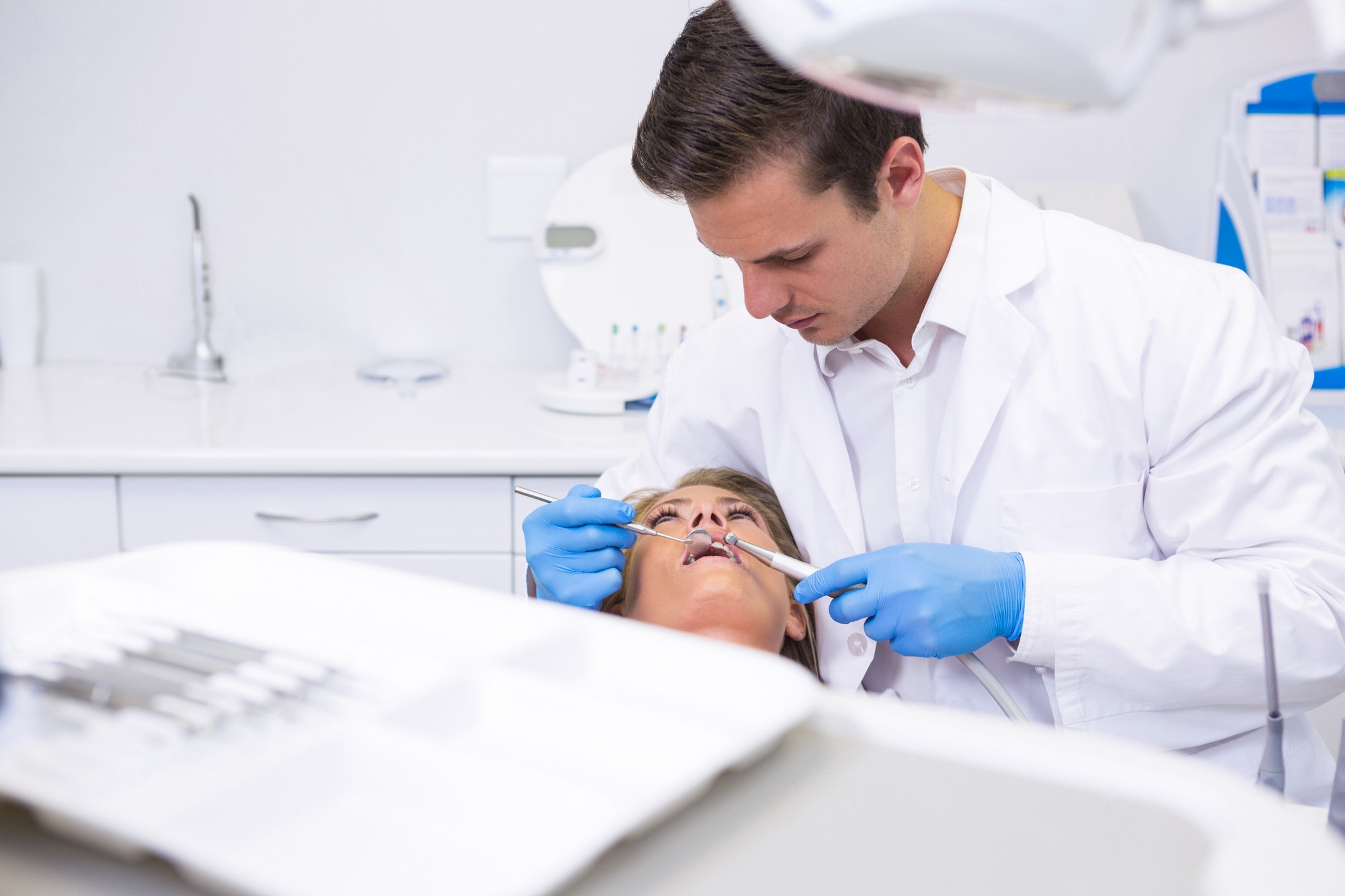 Dentist holding medical equipment while giving treatment to woman