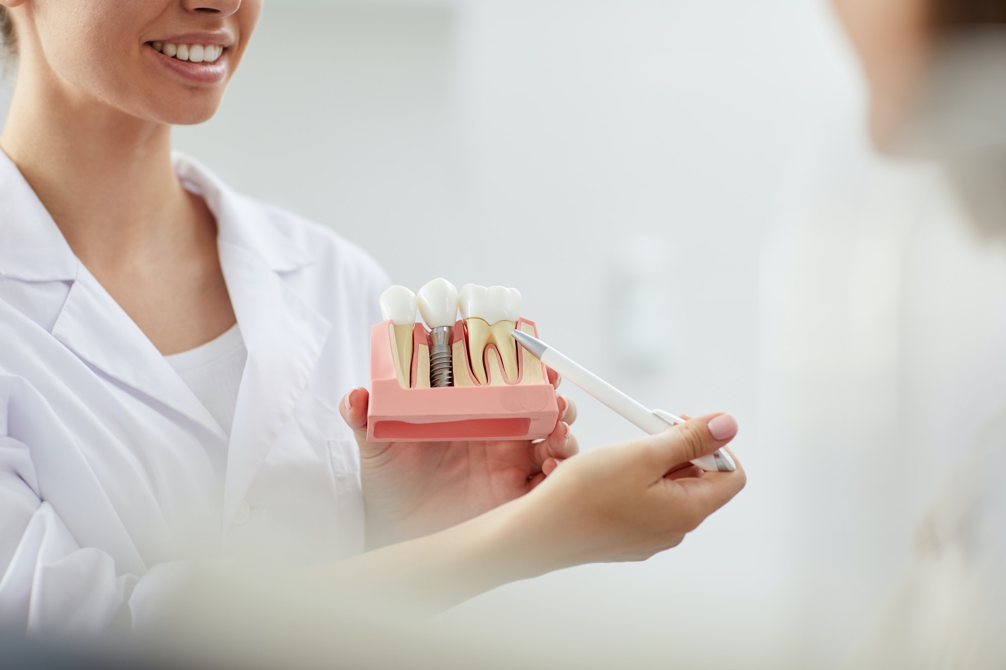 Smiling Dentist Pointing at Tooth Model